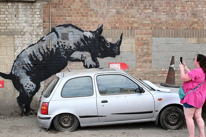 Lundi encore, un rhinocéros peint semblait escalader une voiture abandonnée dans un terrain vague. © KEYSTONE/EPA/ANDY RAIN